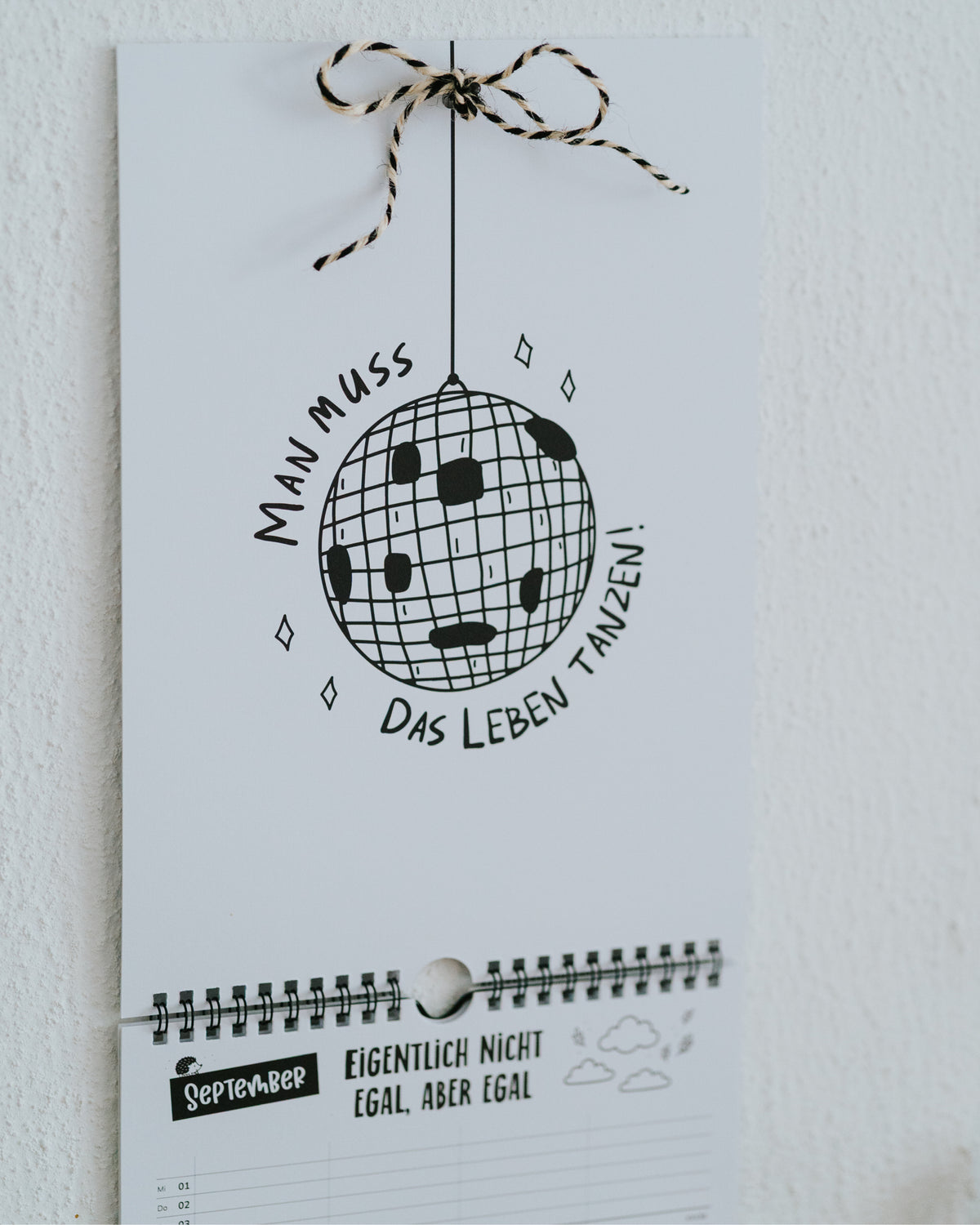 September-Seite des Familienkalenders mit Discokugel-Illustration und Spruch, Aufhängeschleife aus schwarz-weißer Kordel.