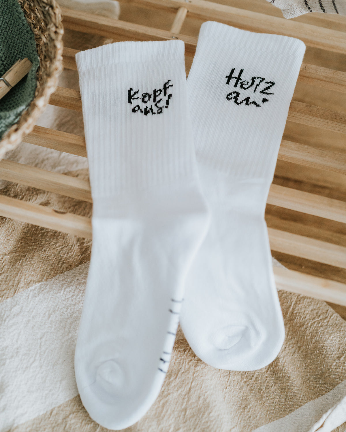 Sockenpaar „Kopf aus!“ und „Herz an.“ auf Holzleiste – stilvolles Schwarz-Weiß-Design.