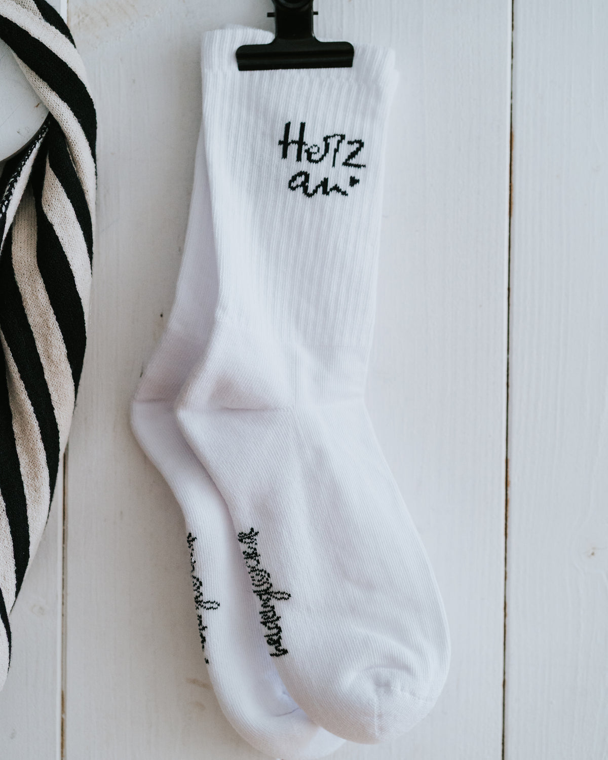 Einzelner Socken „Herz an.“ an weißer Wand – Größen 35–38 oder 39–42.