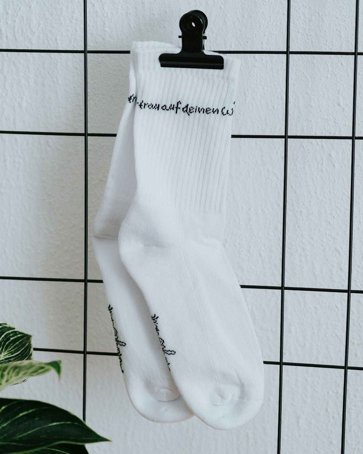 Einzelner Socken an weißer Fliesenwand mit schwarzer Klammer.