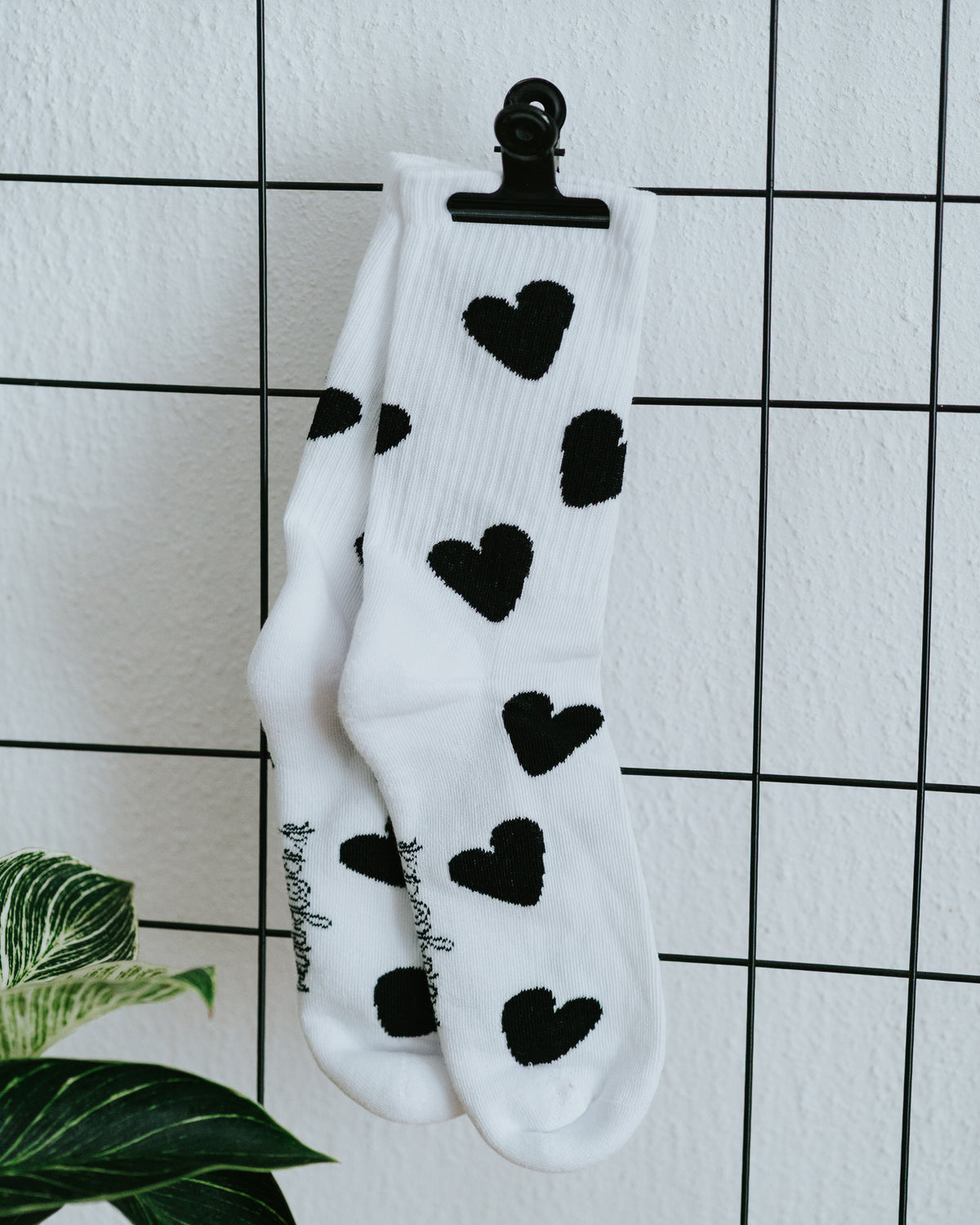 Einzelner Herz-Socken an weißer Fliesenwand mit schwarzer Klammer.