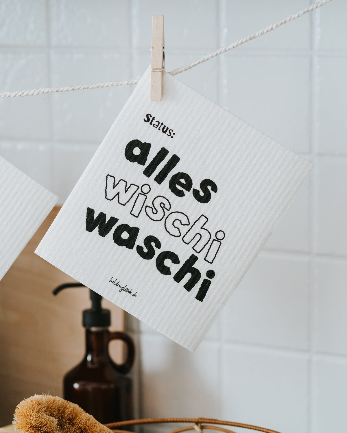 Schwammtuch „Status: alles wischi waschi“ an der Holzklammer.