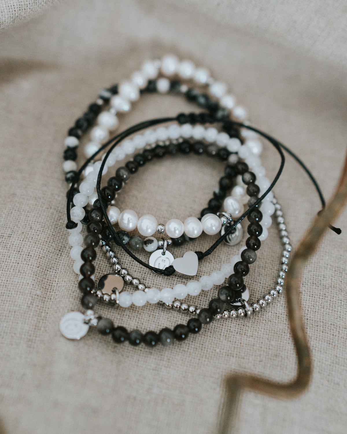 Baumwoll-Armband flach auf Leinen neben Perlen- und Obsidian-Armbändern.
