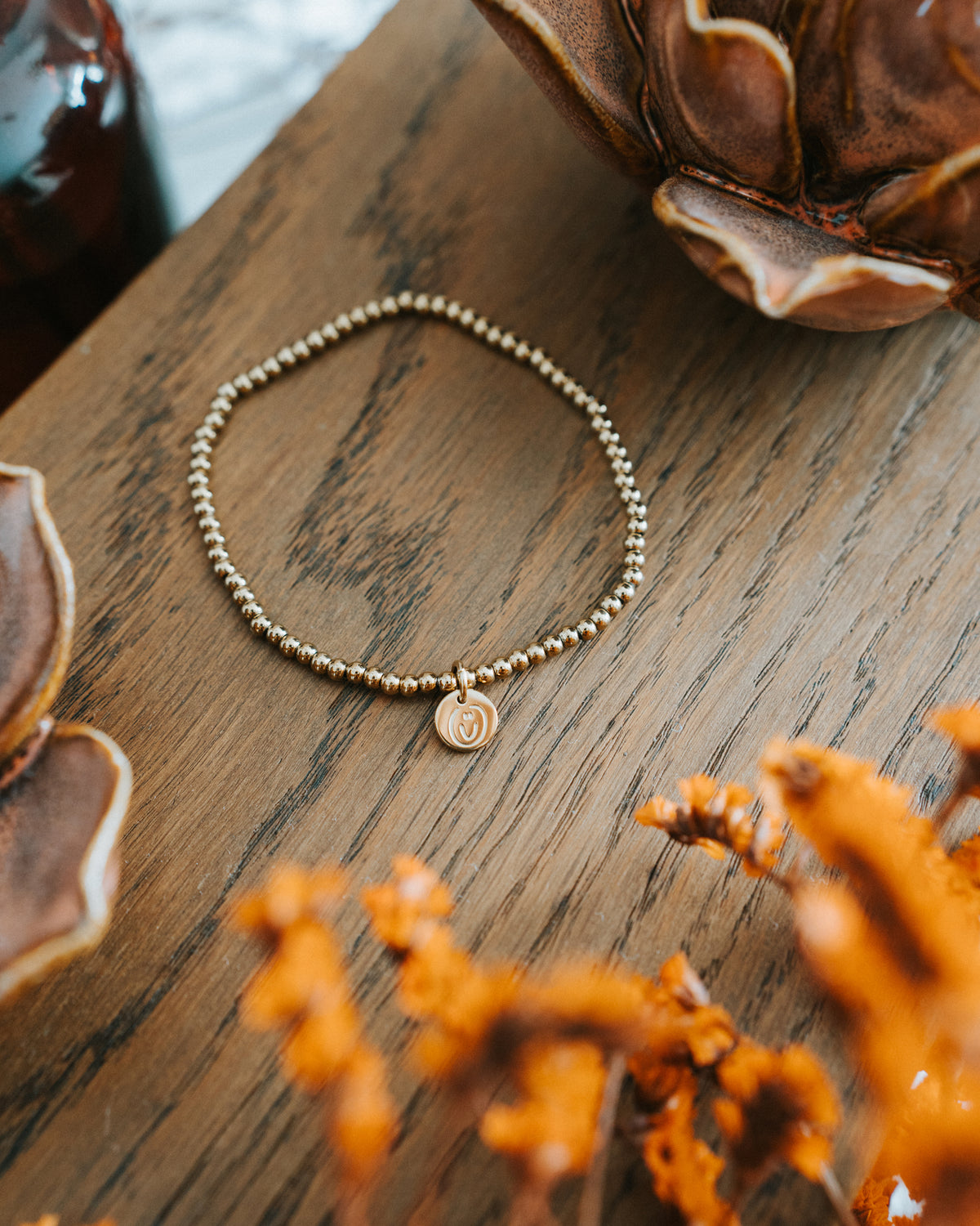 Edelstahl-Armband in Gold auf Holz – Edelstahlkugeln mit Logo-Plättchen.