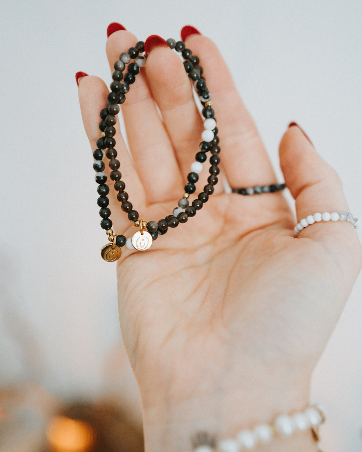 Hand hält mehrere Armbänder – Obsidian in Gold mit Perlen.
