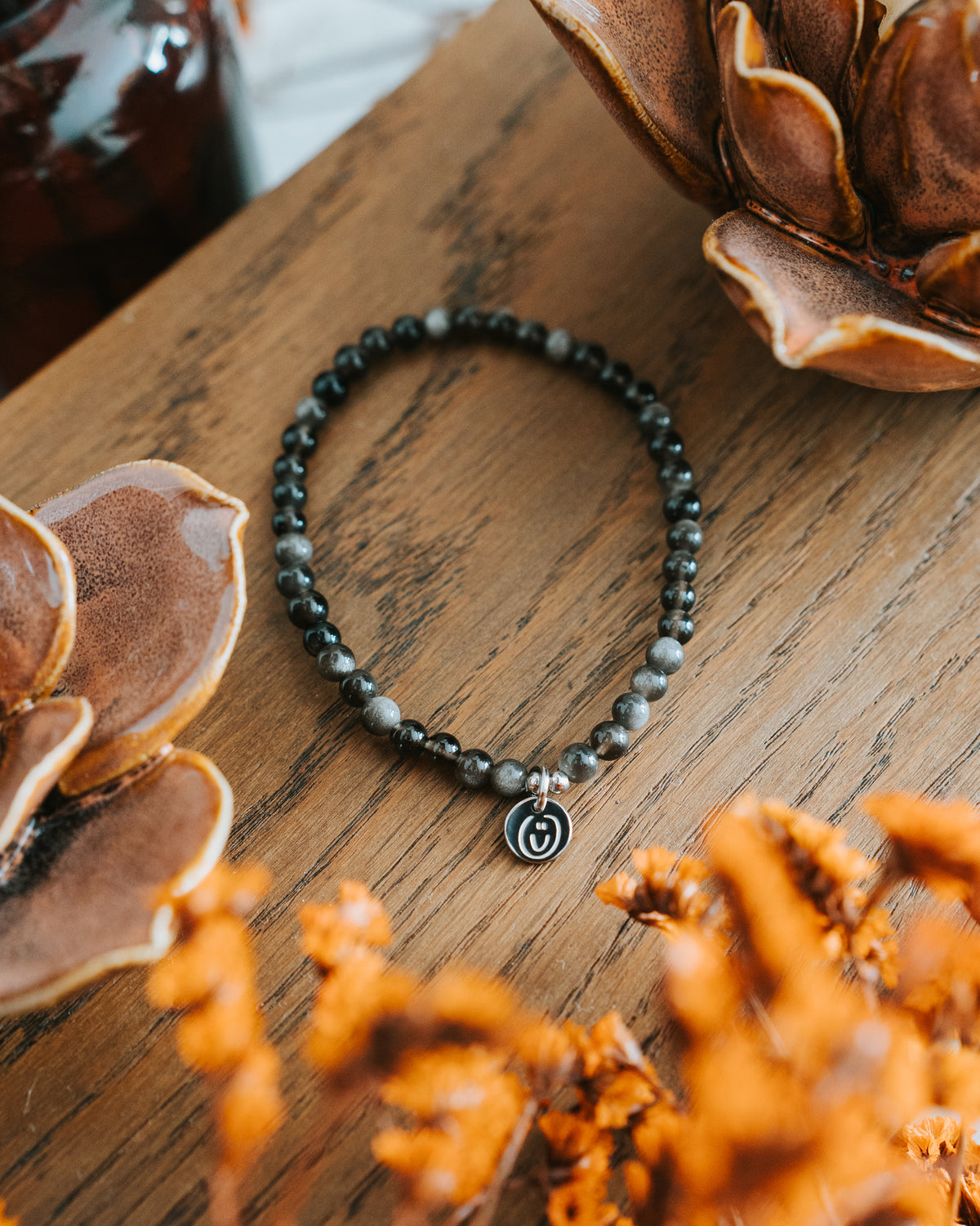 Obsidian-Armband in Silber auf Holz mit Trockenblumen – facettierte Perlen.