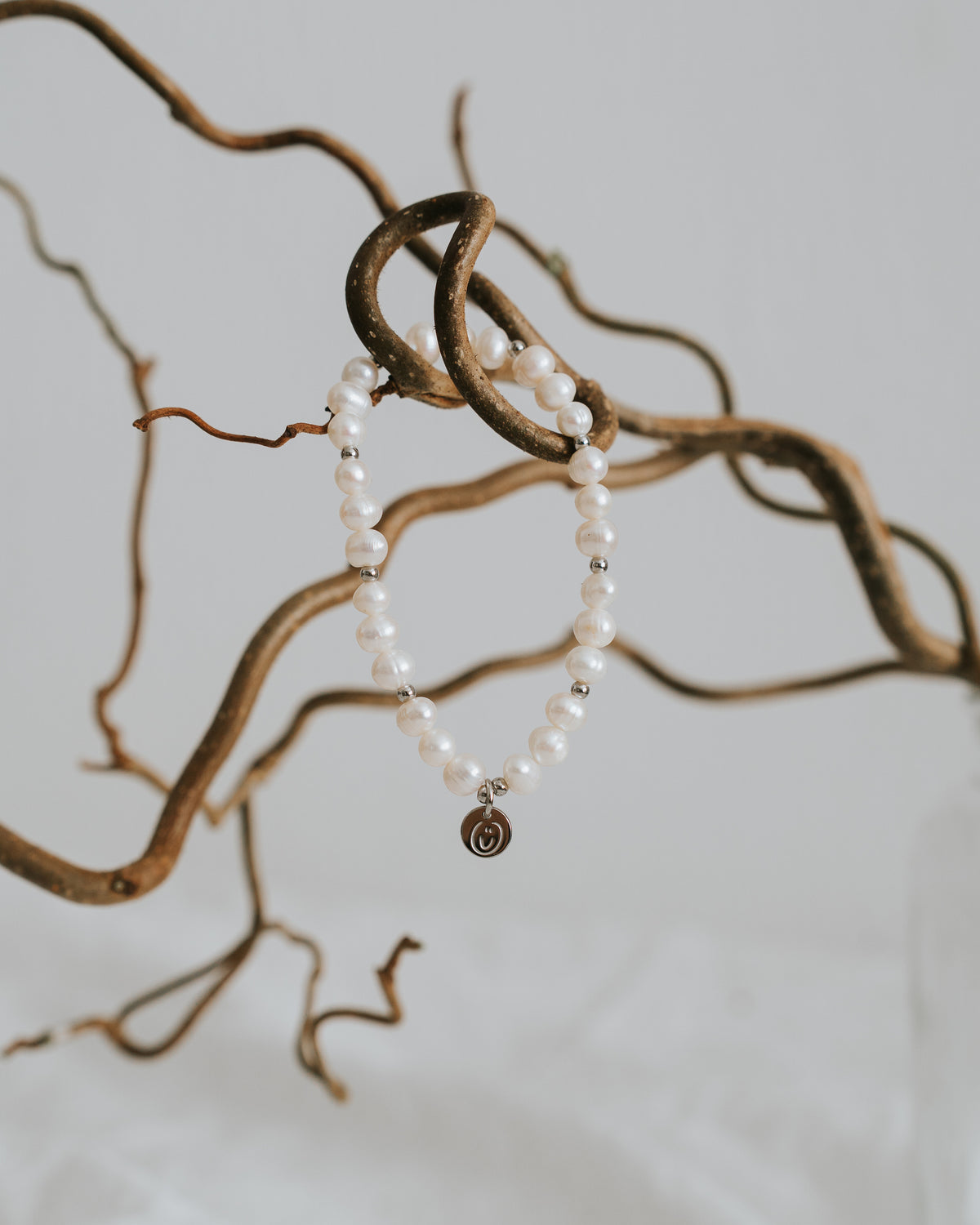 Süßwasserperlen-Armband in Silber zwischen Zweigen.
