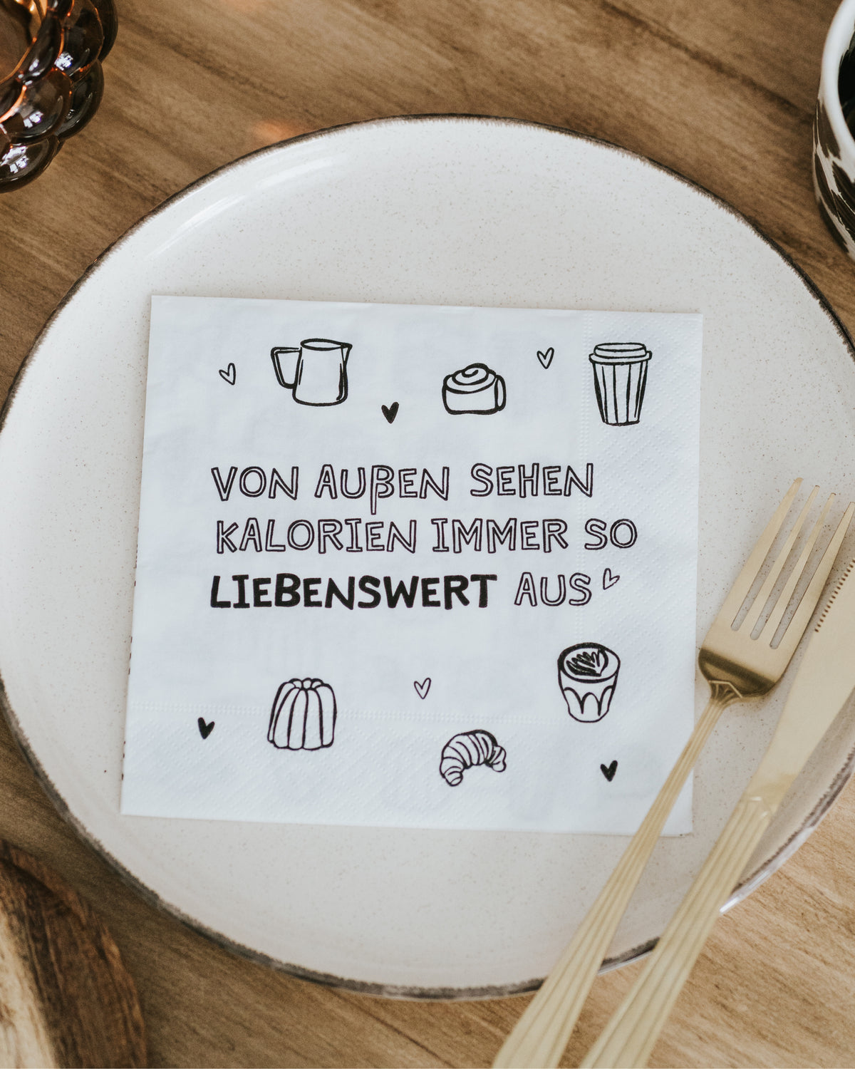 Serviette mit Spruch „Von außen sehen Kalorien immer so liebenswert aus“ auf gedecktem Tisch.