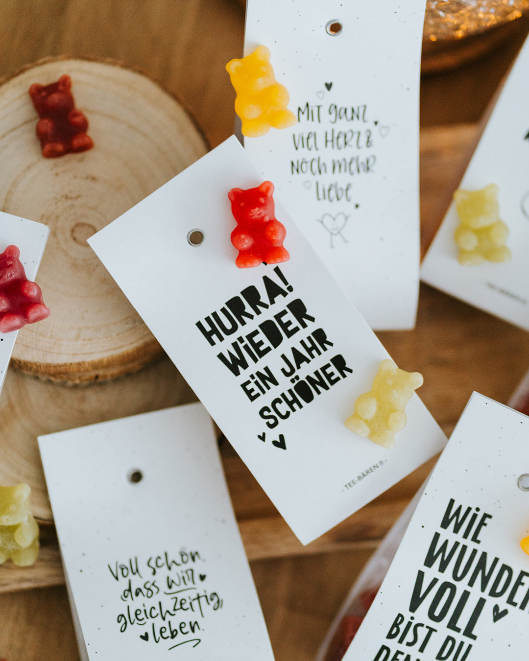 Draufsicht auf mehrere Teebären-Motive mit Fruchtgummi-Bärchen auf Holztisch.