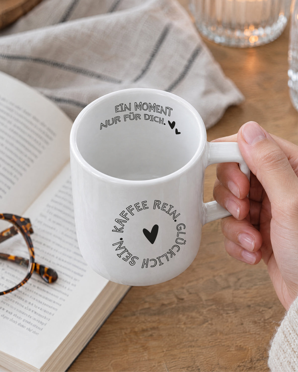 Hand hält Porzellantasse über einem Buch, zweiter Spruch am Trinkrand – „Ein Moment nur für dich“.