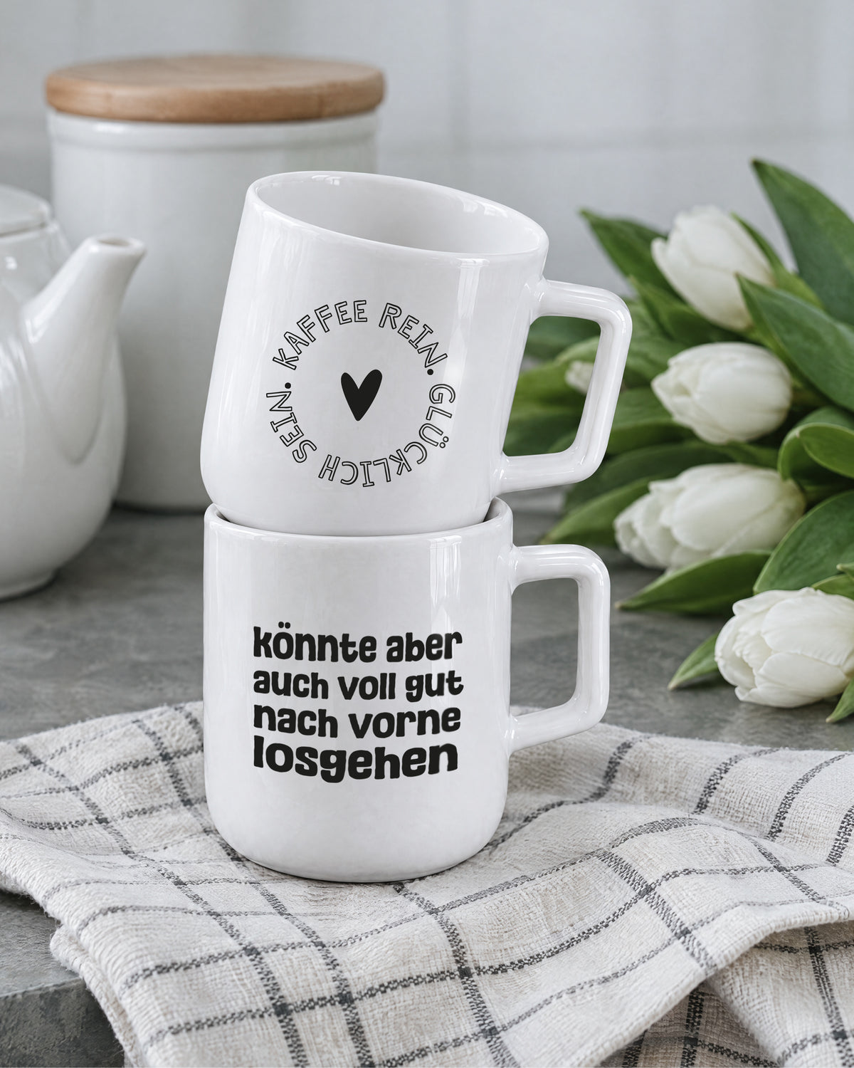 Zwei gestapelte Porzellantassen neben Tulpen und Vorratsdose – Porzellan mit Henkel.