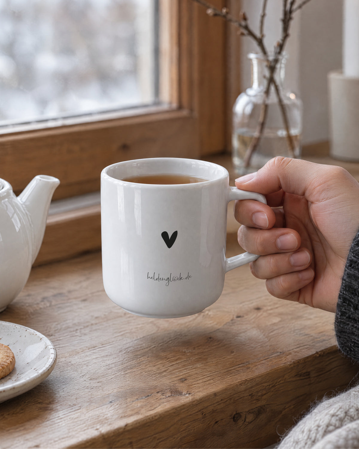 Hand hält Porzellantasse mit Kaffee am Fenster – weißes Porzellan mit Henkel.