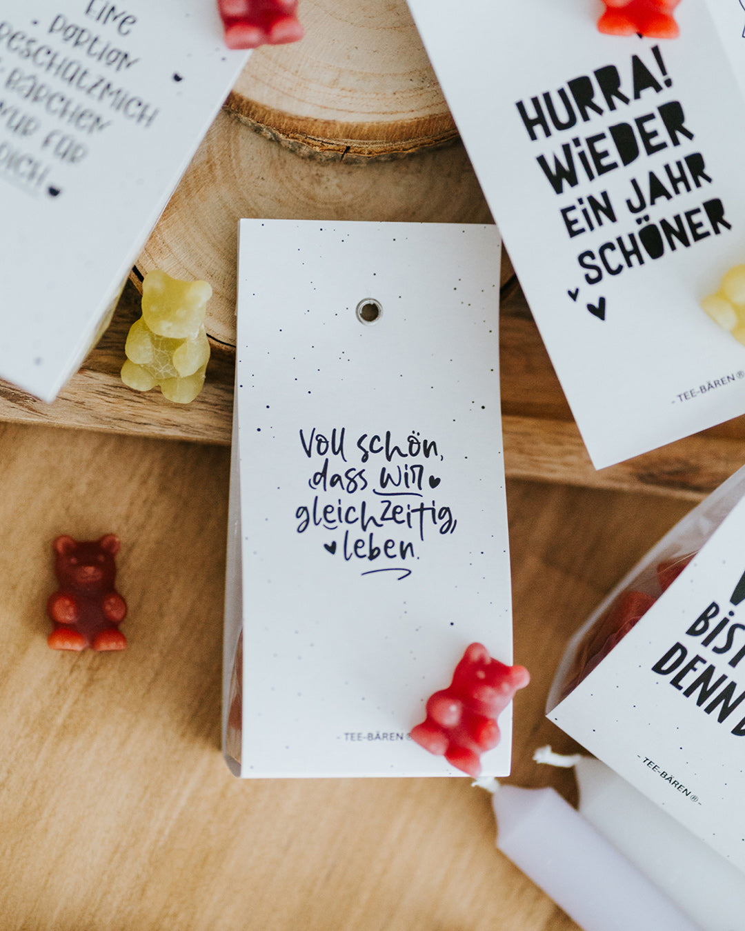 Teebären Voll schön liegend auf Holzscheibe, bunte Fruchtgummi-Bärchen verstreut.