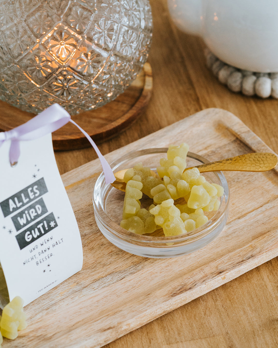 Limettengrüne Fruchtgummi-Bärchen in der Glasschale mit Goldlöffel vor Windlicht.