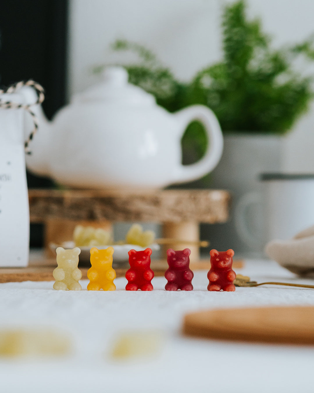 Fünf Fruchtgummi-Bärchen in allen Sorten in einer Reihe vor weißer Teekanne.
