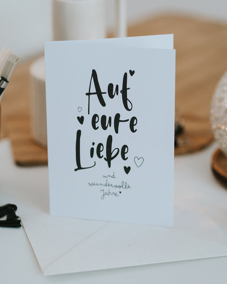 Hochzeitskarte „Auf eure Liebe" aufgestellt vor passendem Umschlag, zeitloses Schwarz-Weiß-Design