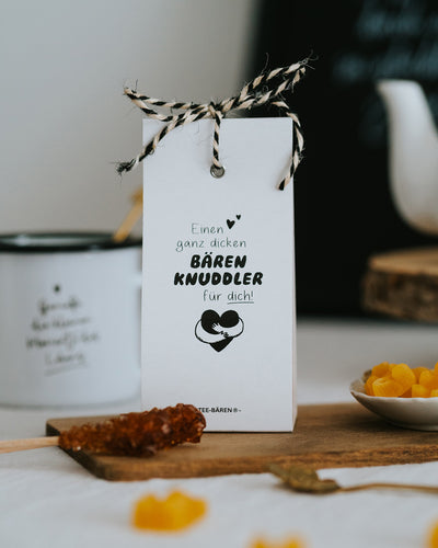 Teebären Bärenknuddler auf gedecktem Tisch mit Emaillebecher, Kandiszucker und Bärchen im Schälchen.