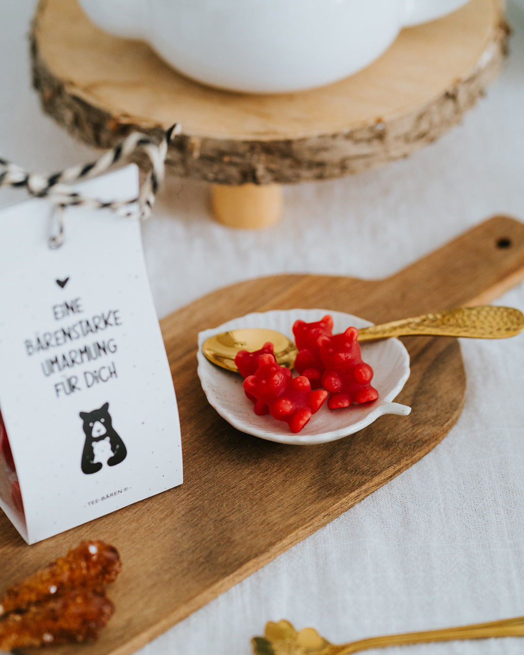Rote Fruchtgummi-Bärchen im Schälchen mit Goldlöffel, Teebären-Tüte links angeschnitten.