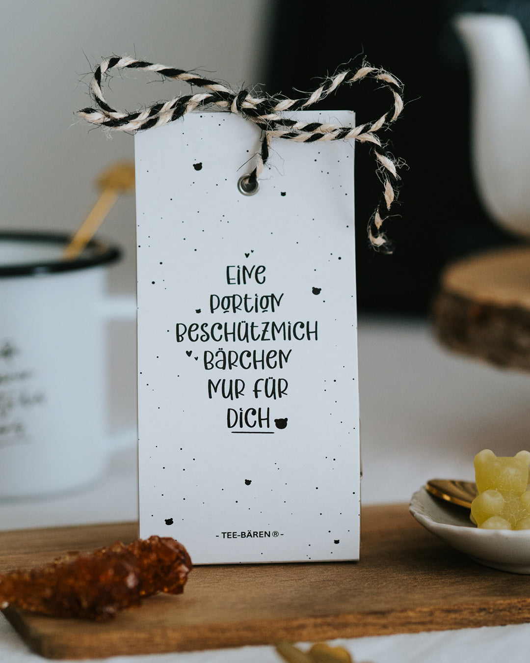 Teebären Beschützmich-Bärchen mit schwarz-weißer Kordel auf Holzbrett, Handlettering in Schwarz.