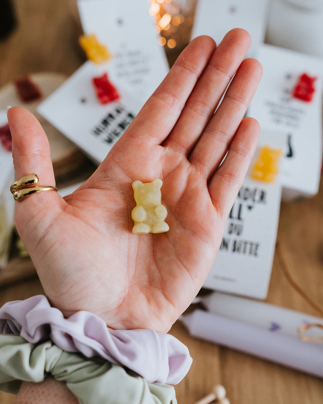Hand hält ein limettengrünes Teebärchen als Größenreferenz, Motive im Hintergrund.