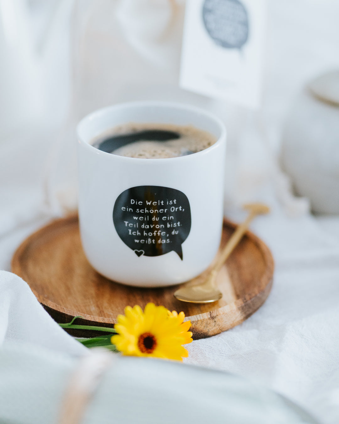Porzellanbecher „Die Welt ist ein schöner Ort“ mit Kaffee auf Holzteller – ideal für Kaffee oder Tee.