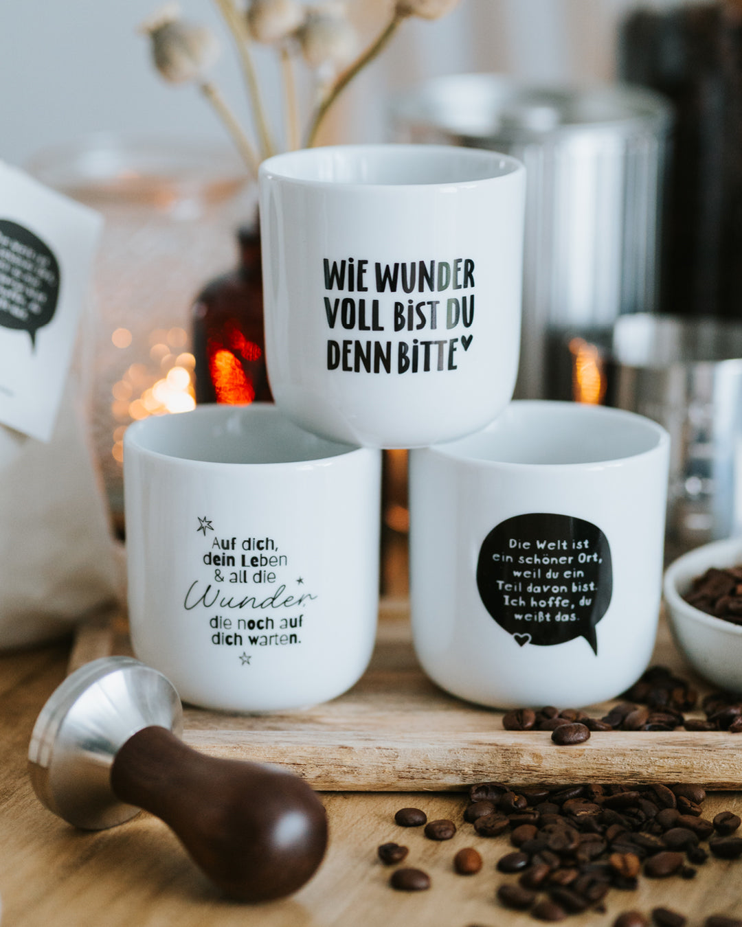 Drei Porzellanbecher vor Windlichtern, „Die Welt ist ein schöner Ort“ rechts.