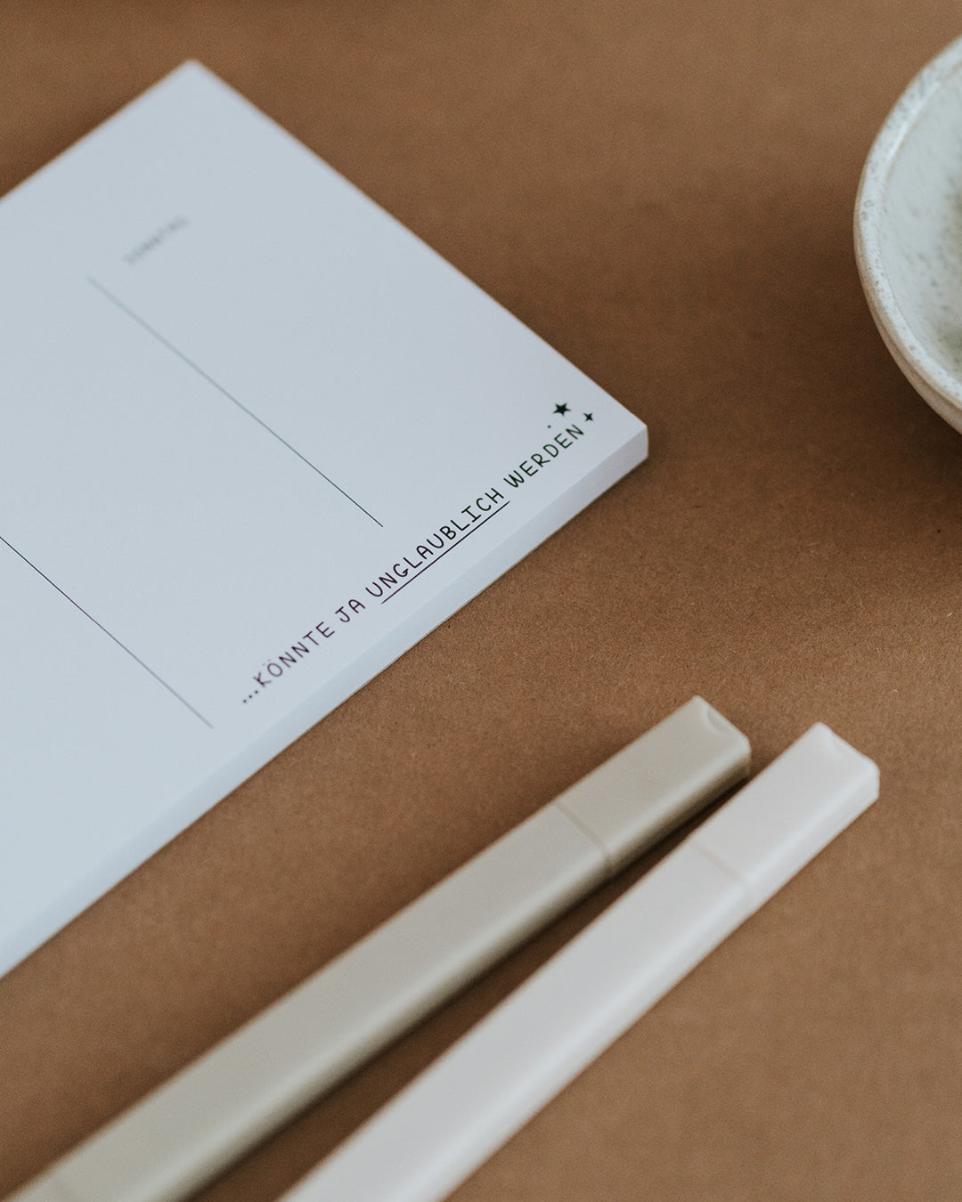 Detail des Wochenplaners mit Schriftzug „…könnte ja unglaublich werden" auf dickem Papierblock