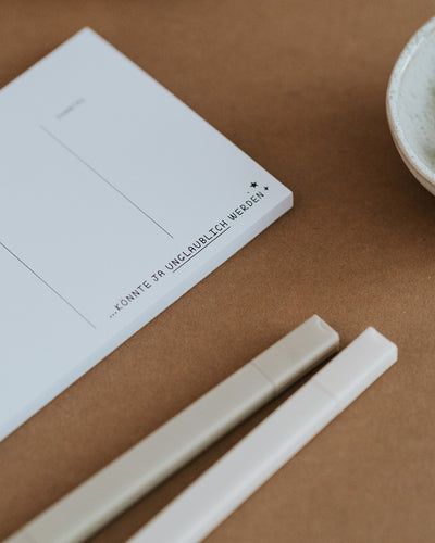 Detail des Wochenplaners mit Schriftzug „…könnte ja unglaublich werden" auf dickem Papierblock