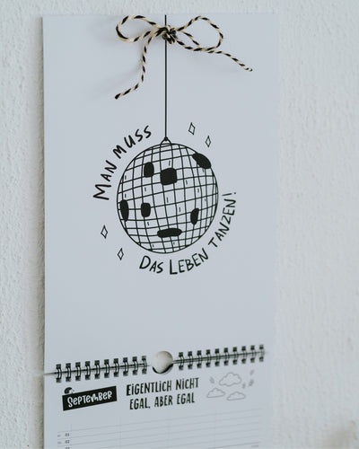September-Seite des Familienkalenders mit Discokugel-Illustration und Spruch, Aufhängeschleife aus schwarz-weißer Kordel.