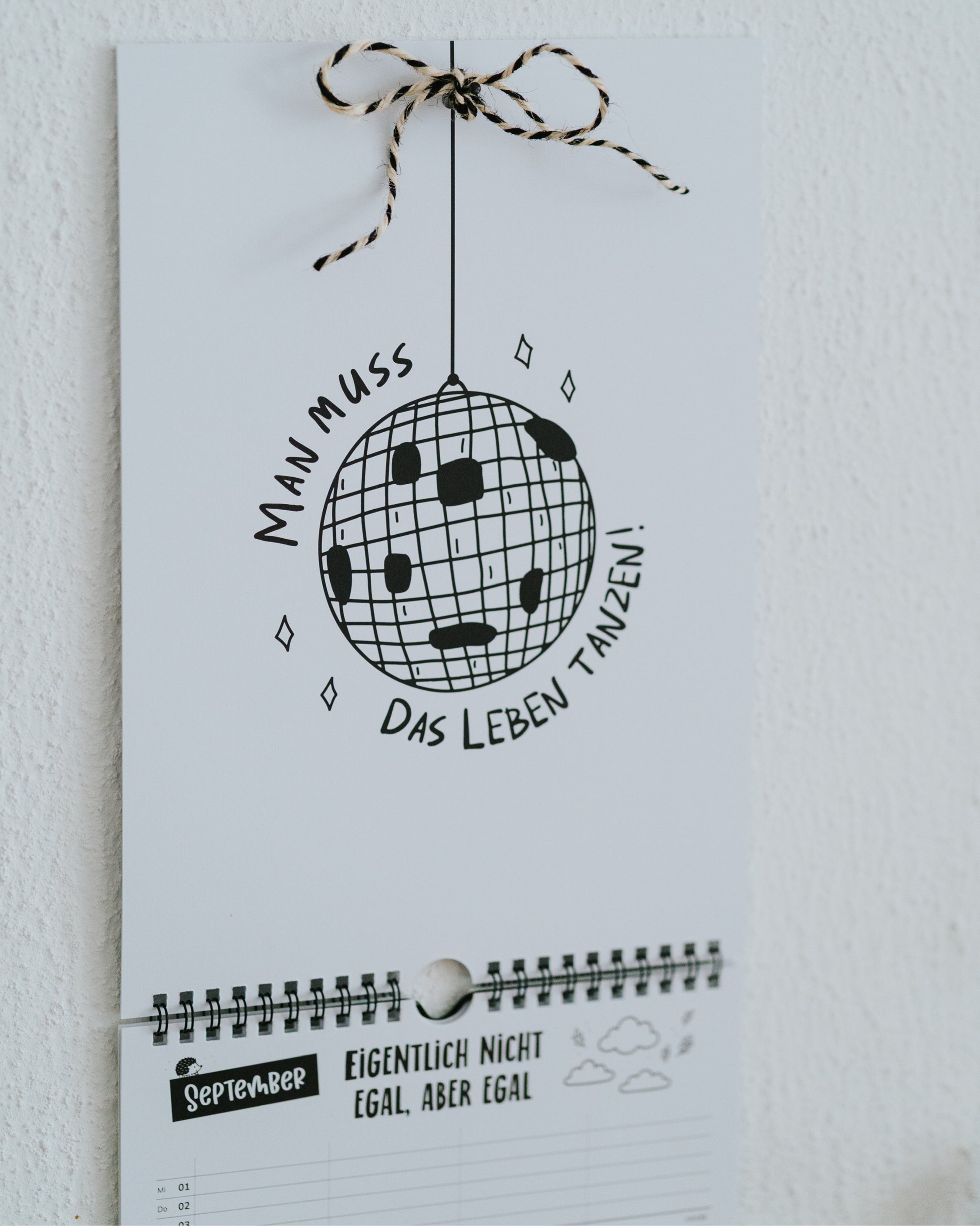 September-Seite des Familienkalenders mit Discokugel-Illustration und Spruch, Aufhängeschleife aus schwarz-weißer Kordel.