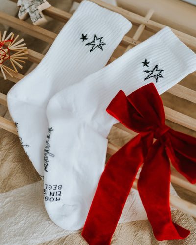 Weiße Socken mit Sternmotiv vor roter Samtschleife – stilvolles Schwarz-Weiß-Design.