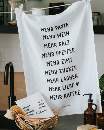 Geschirrtuch mit „Mehr Pasta, mehr Wein, mehr Kaffee“ an der Spüle.