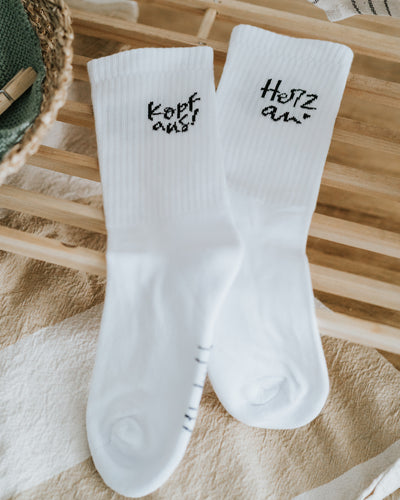Sockenpaar „Kopf aus!“ und „Herz an.“ auf Holzleiste – stilvolles Schwarz-Weiß-Design.