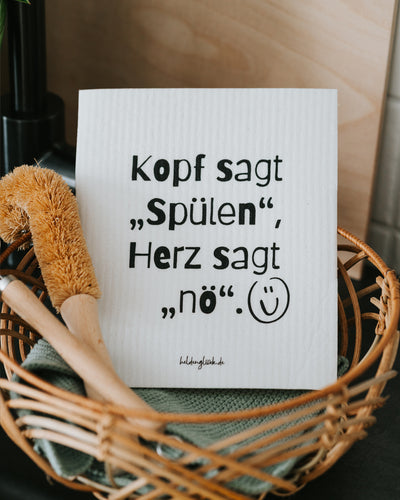 Schwammtuch im Korb mit Spülbürste, Geschirrtuch dahinter.