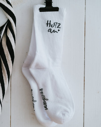 Einzelner Socken „Herz an.“ an weißer Wand – Größen 35–38 oder 39–42.