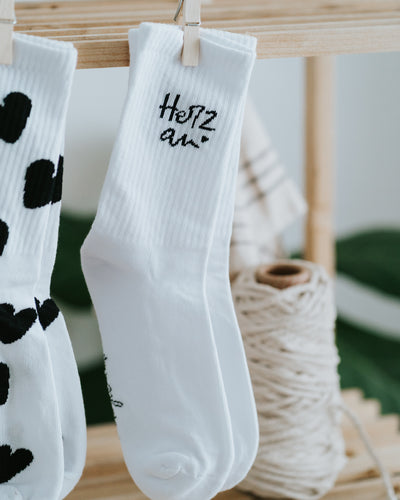 Socken „Herz an.“ am Holzregal, Herz-Socken im Hintergrund.