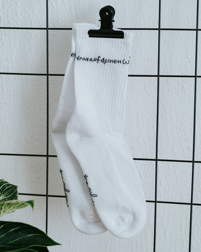 Einzelner Socken an weißer Fliesenwand mit schwarzer Klammer.