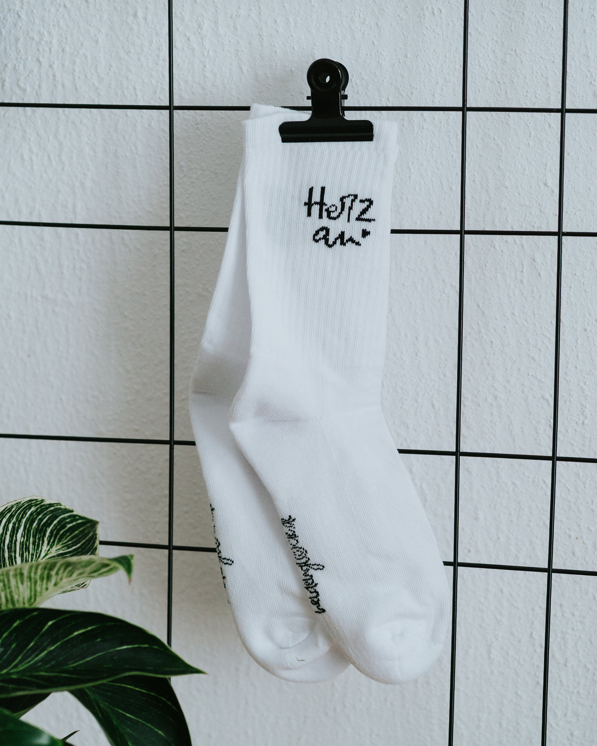 Socken an weißer Fliesenwand mit schwarzer Klammer – verstärkte Innenfrottee-Sohle.
