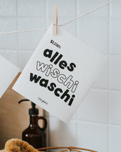 Schwammtuch „Status: alles wischi waschi“ an der Holzklammer.