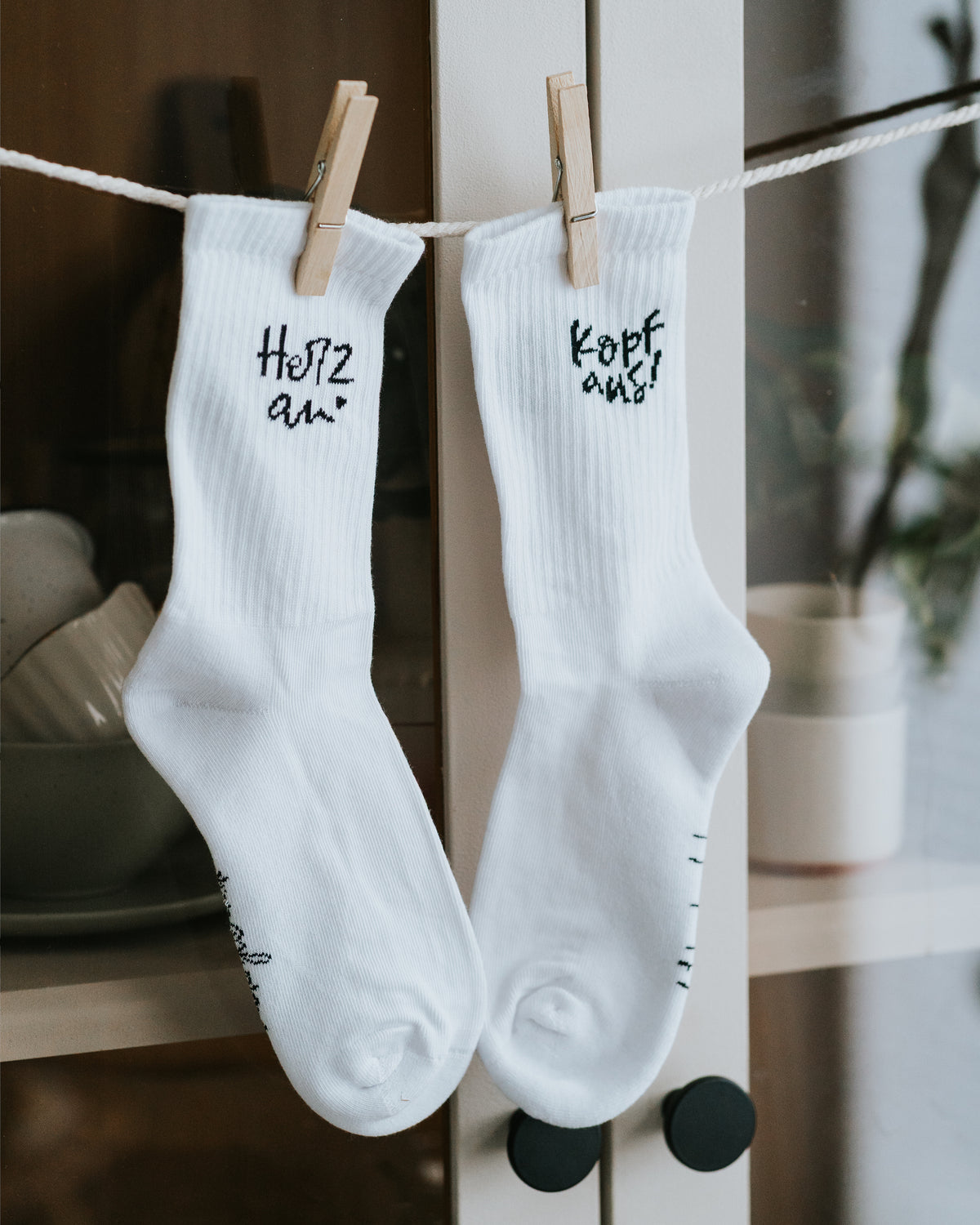 Sockenpaar „Herz an.“ und „Kopf aus!“ hängend im Raum.