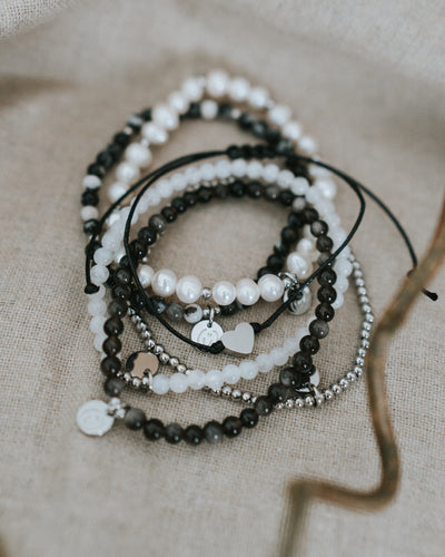 Baumwoll-Armband flach auf Leinen neben Perlen- und Obsidian-Armbändern.