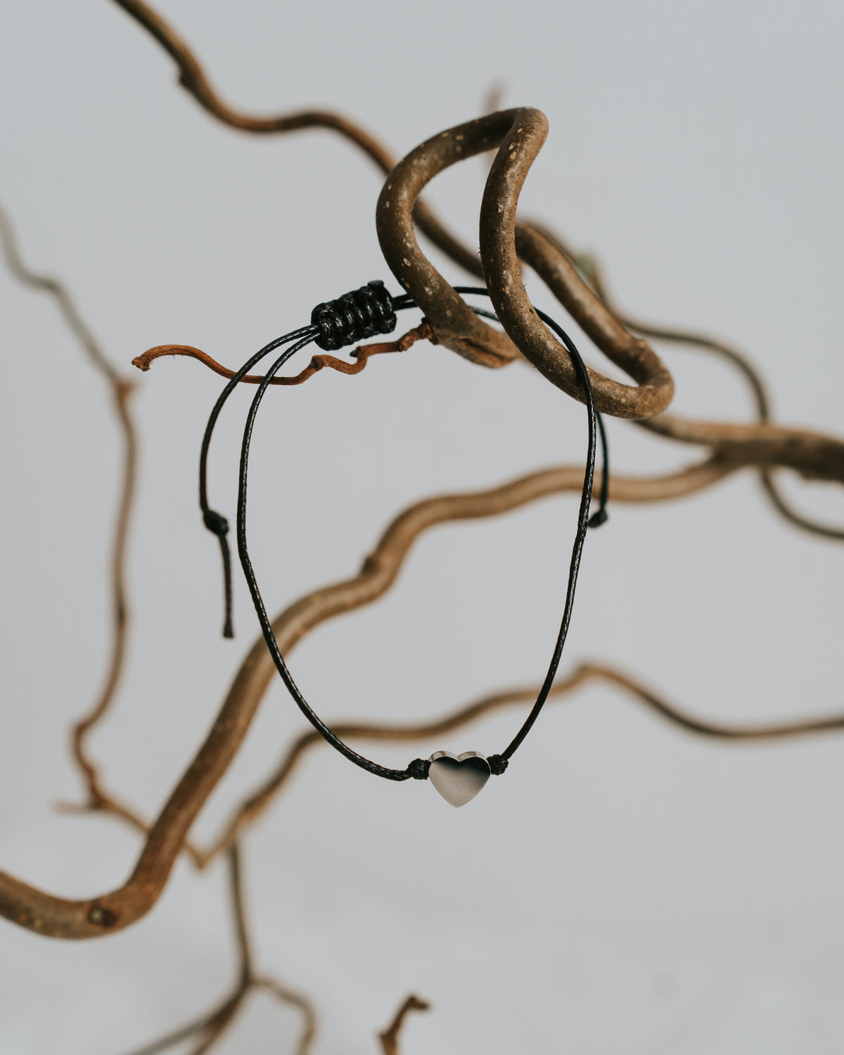 Baumwoll-Armband mit silbernem Herz zwischen Zweigen.