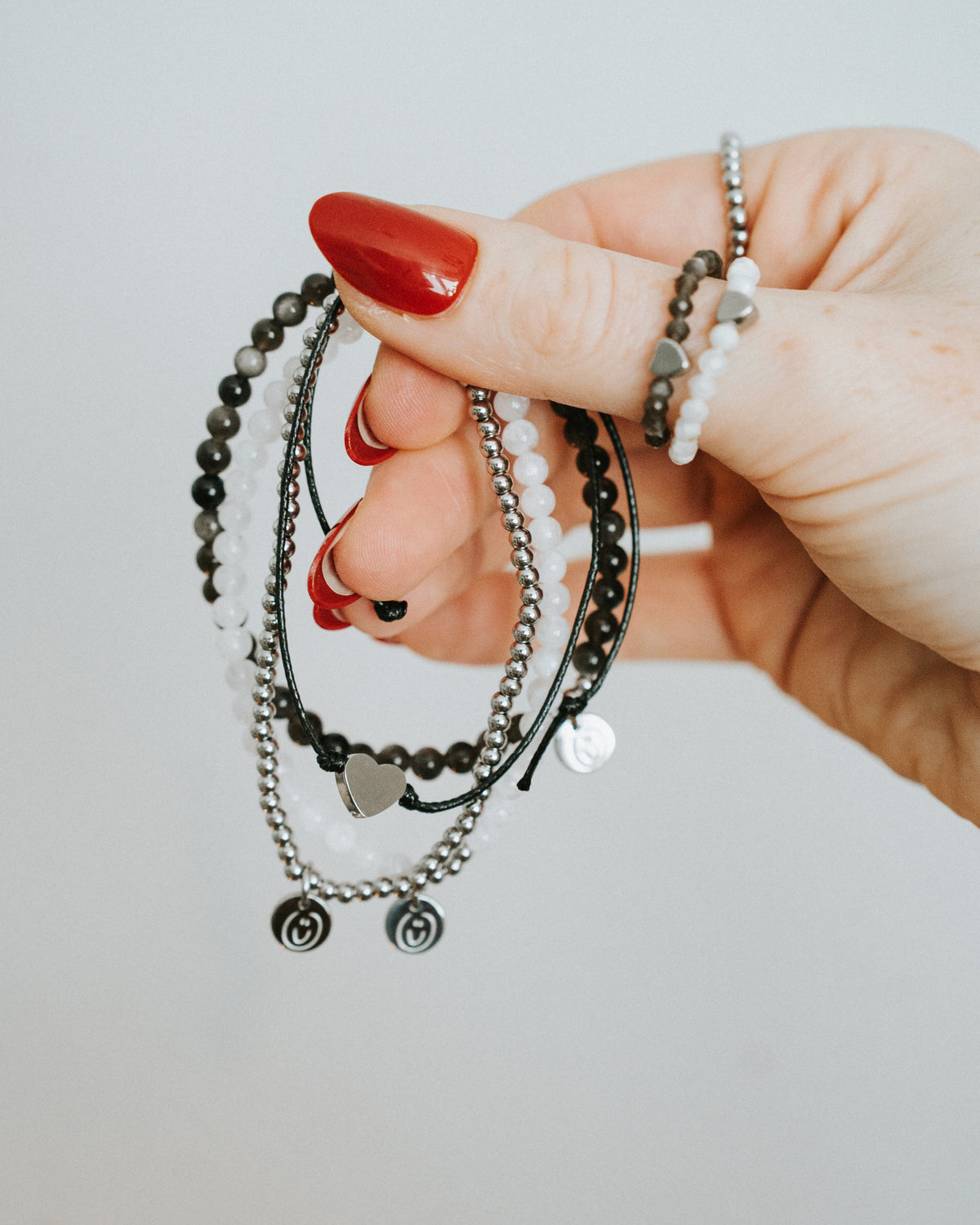 Hand hält Baumwoll-Armband mit silbernem Herz.