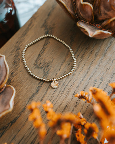 Edelstahl-Armband in Gold auf Holz – Edelstahlkugeln mit Logo-Plättchen.