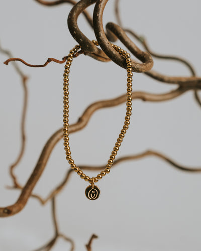 Edelstahl-Armband in Gold zwischen Zweigen, Anhänger sichtbar.