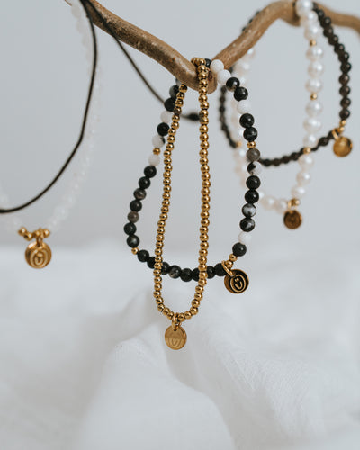 Edelstahl-Armband in Gold flach neben Naturstein-Armbändern.