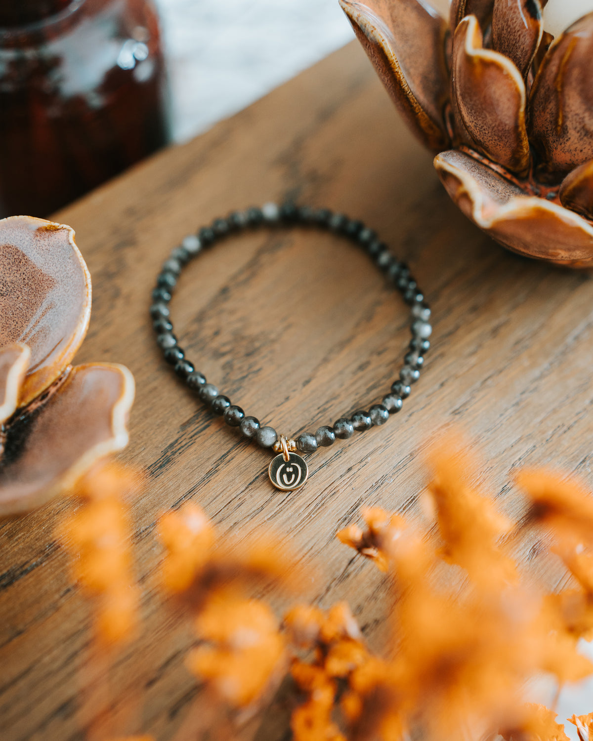 Obsidian-Armband in Gold auf Holz mit Trockenblume.