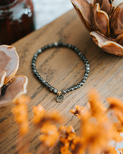 Obsidian-Armband in Gold auf Holz mit Trockenblume.