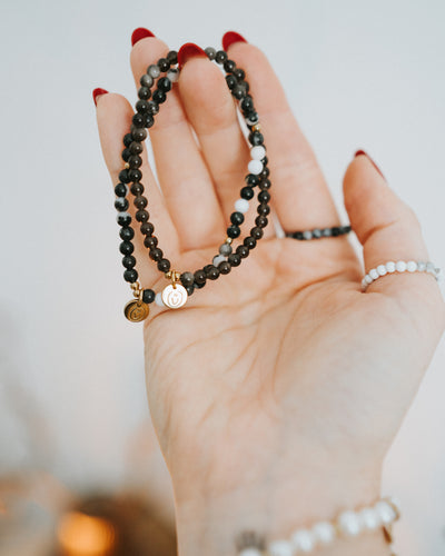 Hand hält mehrere Armbänder – Obsidian in Gold mit Perlen.