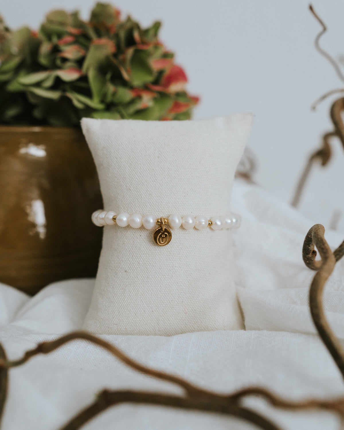 Süßwasserperlen-Armband in Gold am Schmuckständer neben Vase.